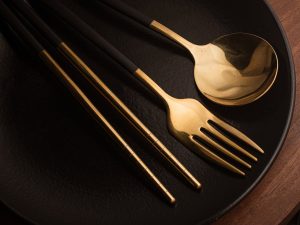 Stylish close-up of modern black and gold cutlery set on ceramic plate.